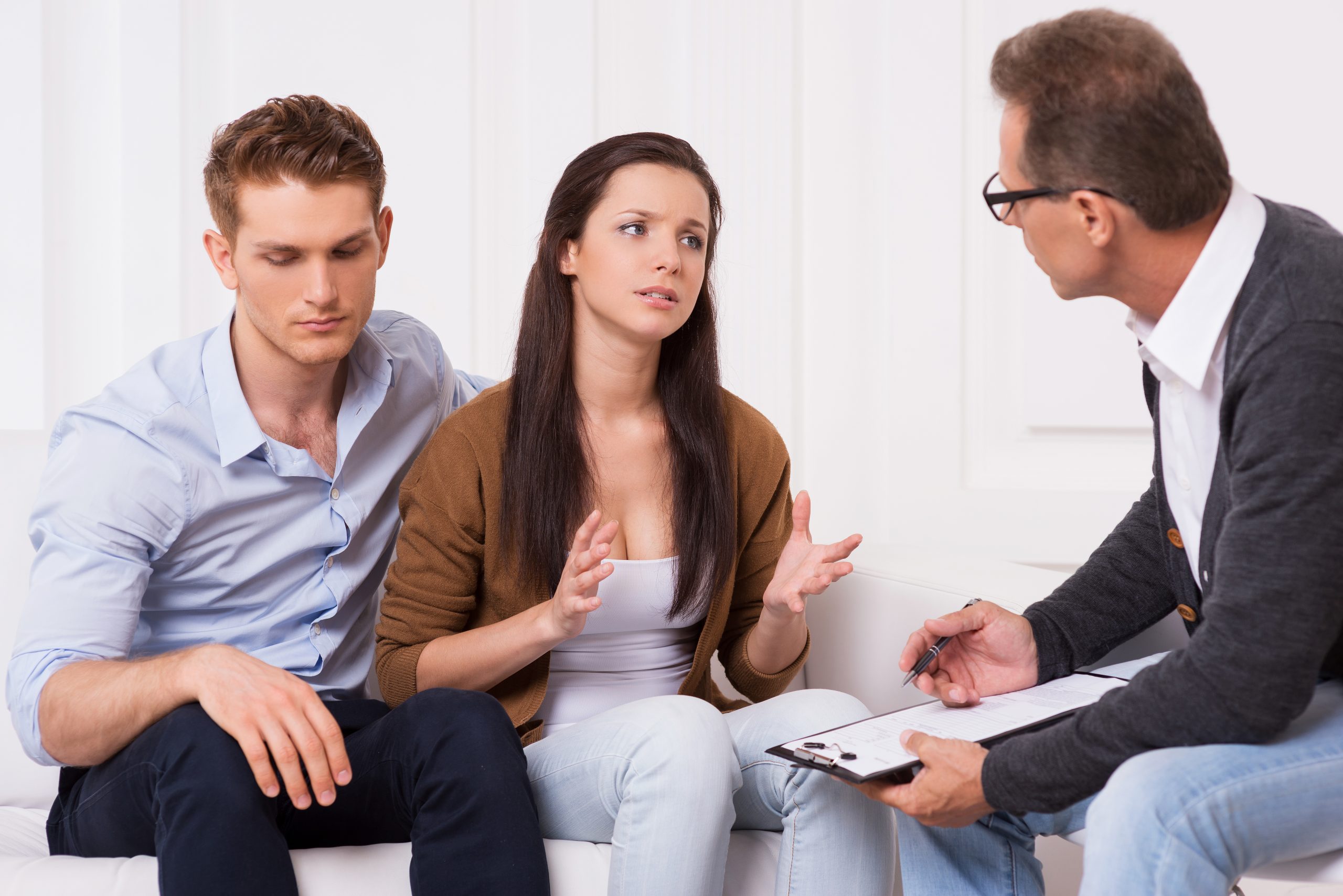 Asking for an expert advice. Frustrated young couple sitting on the couch while woman telling about their relationship problems to psychiatrist and gesturing